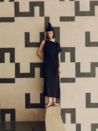 Model wearing black sleeveless dress and beanie posing against patterned tile wall for Massimo Dutti campaign