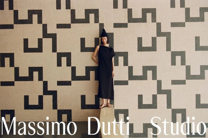 Model in a black dress and beanie standing against a patterned tile wall for Massimo Dutti Studio campaign