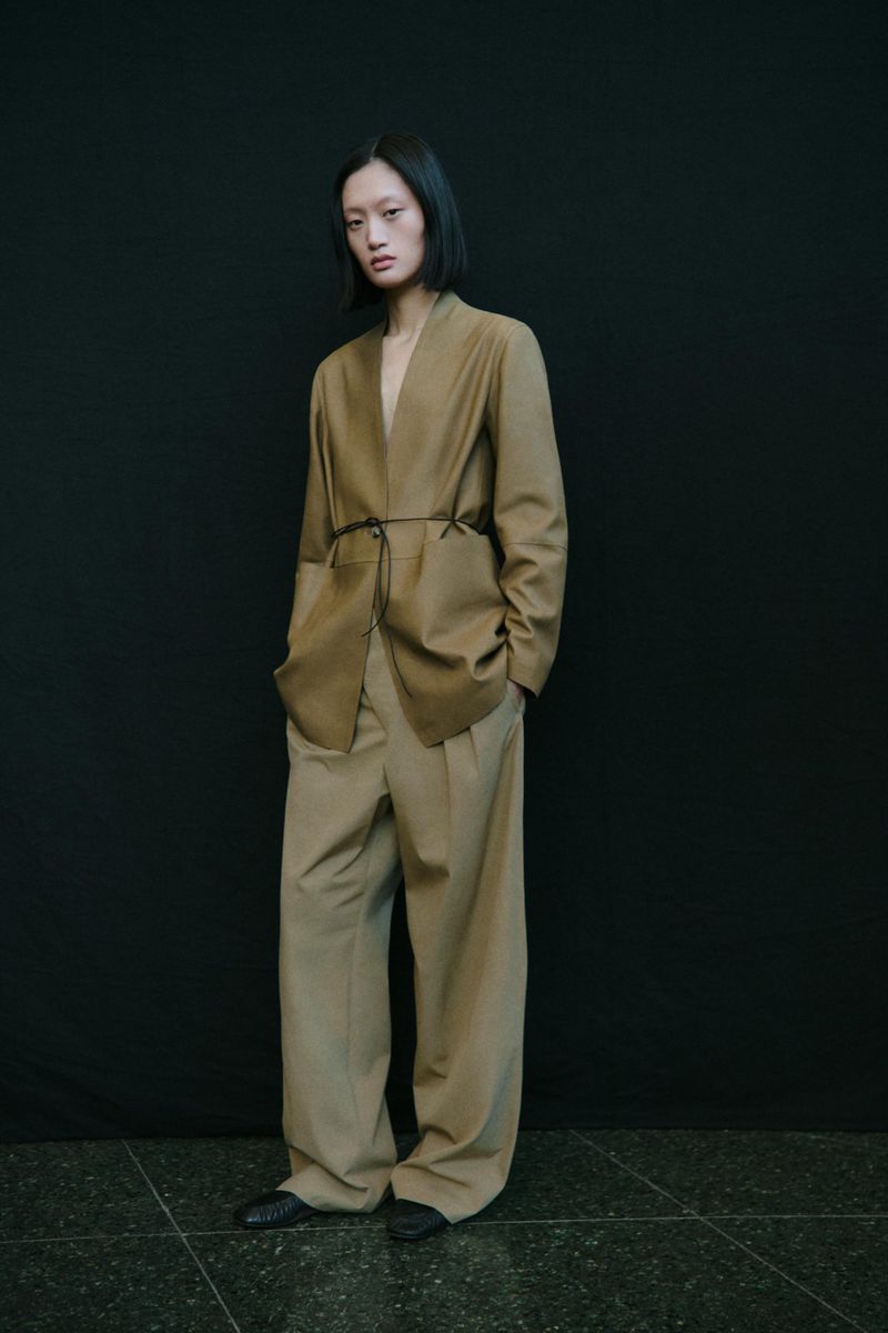 Model Yilan Hua wearing camel-colored blazer and trousers against a dark backdrop for Massimo Dutti Studio campaign.