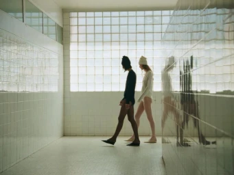 Two models walking in profile down a tiled hallway in front of a large glass block window for Massimo Dutti