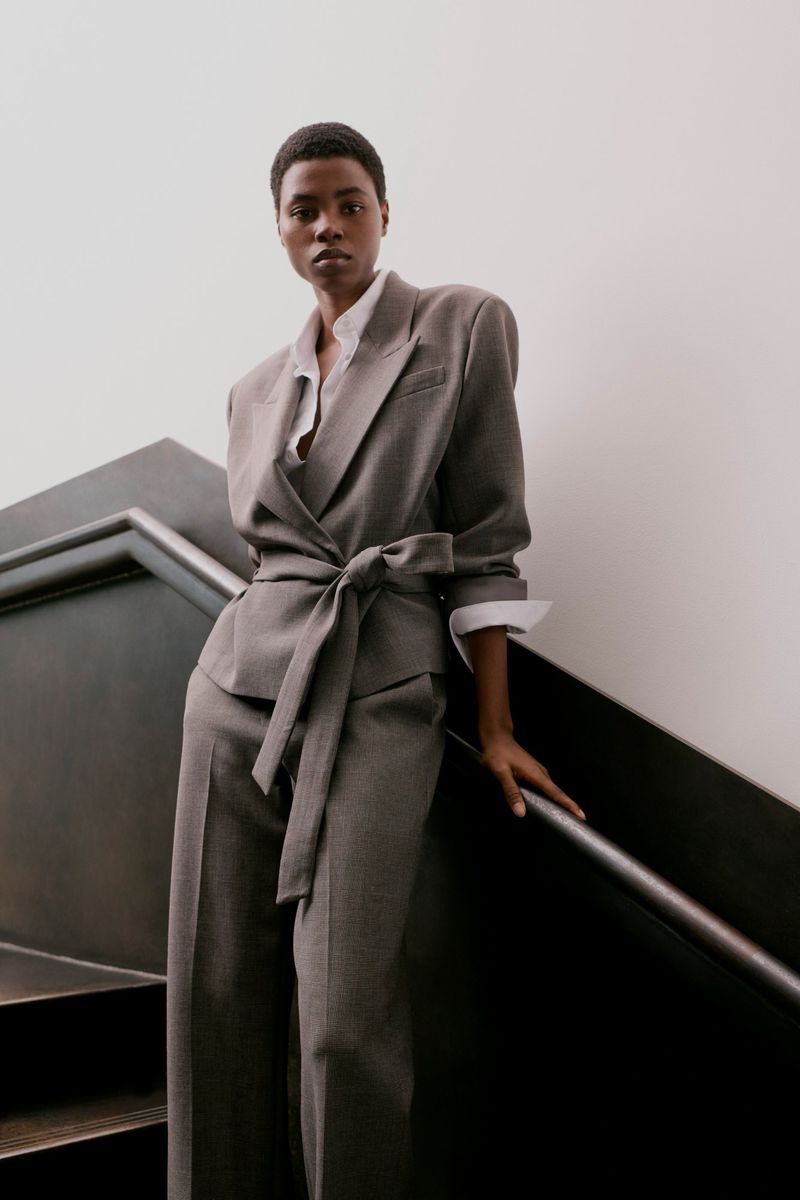 Model Victoria Fawole wearing a grey belted suit jacket and trousers standing near a modern dark handrail.