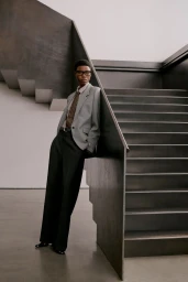 Model wearing a grey blazer and black trousers leaning against a dark staircase for Aritzia