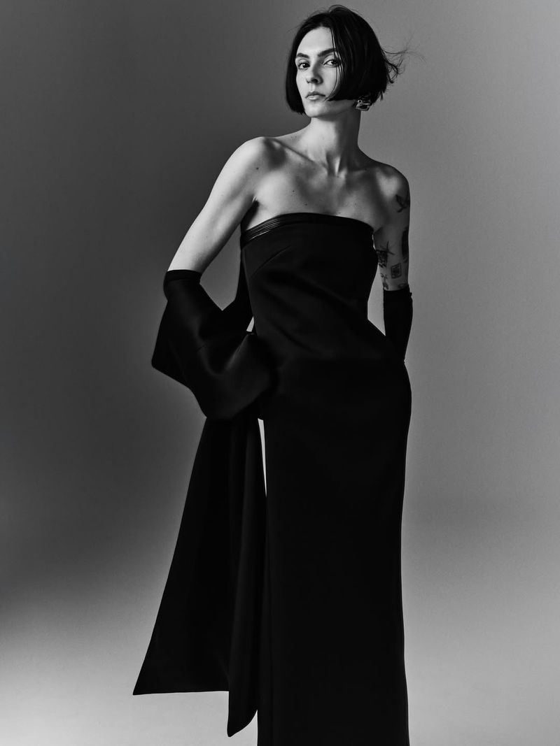 Monochrome fashion portrait of a woman wearing a black strapless gown and long matching gloves against a gradient studio background.
