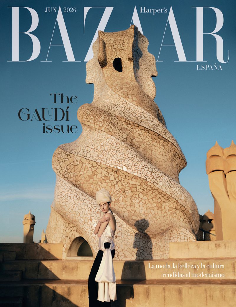 A model standing in front of an intricate stone rooftop structure under a clear blue sky, featured on a magazine cover.
