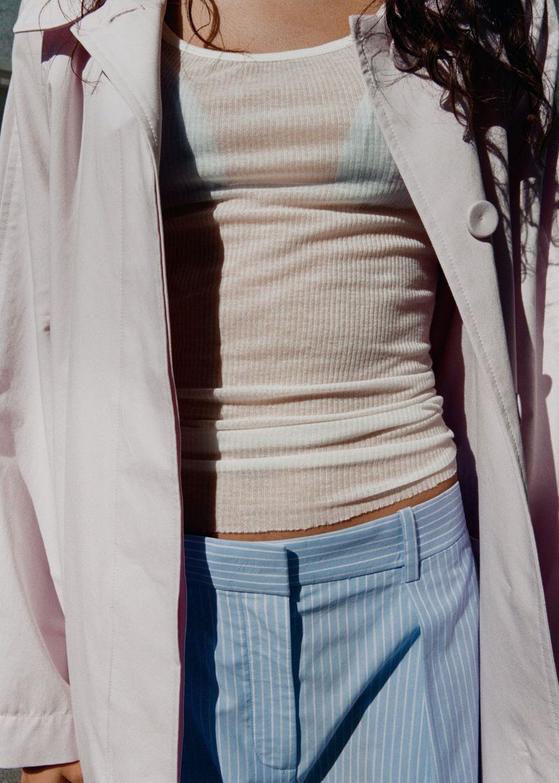 Model wearing a light pink trench coat over a ribbed top and striped trousers for Mango PJ Craft project