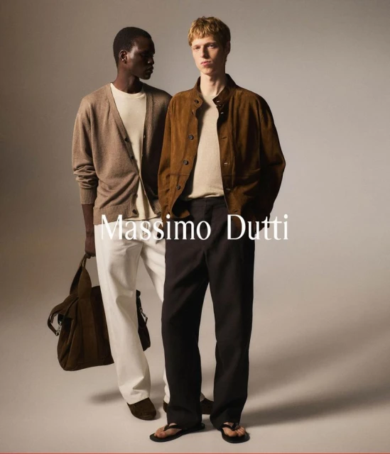 Two male models pose in a studio setting, showcasing Massimo Dutti apparel: a cardigan, suede jacket, trousers, and tote bag.