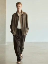 Model Joseph Uyttenhove walking in an open brown suede overshirt, white t-shirt, dark brown trousers, and flip-flops for Massimo Dutti.