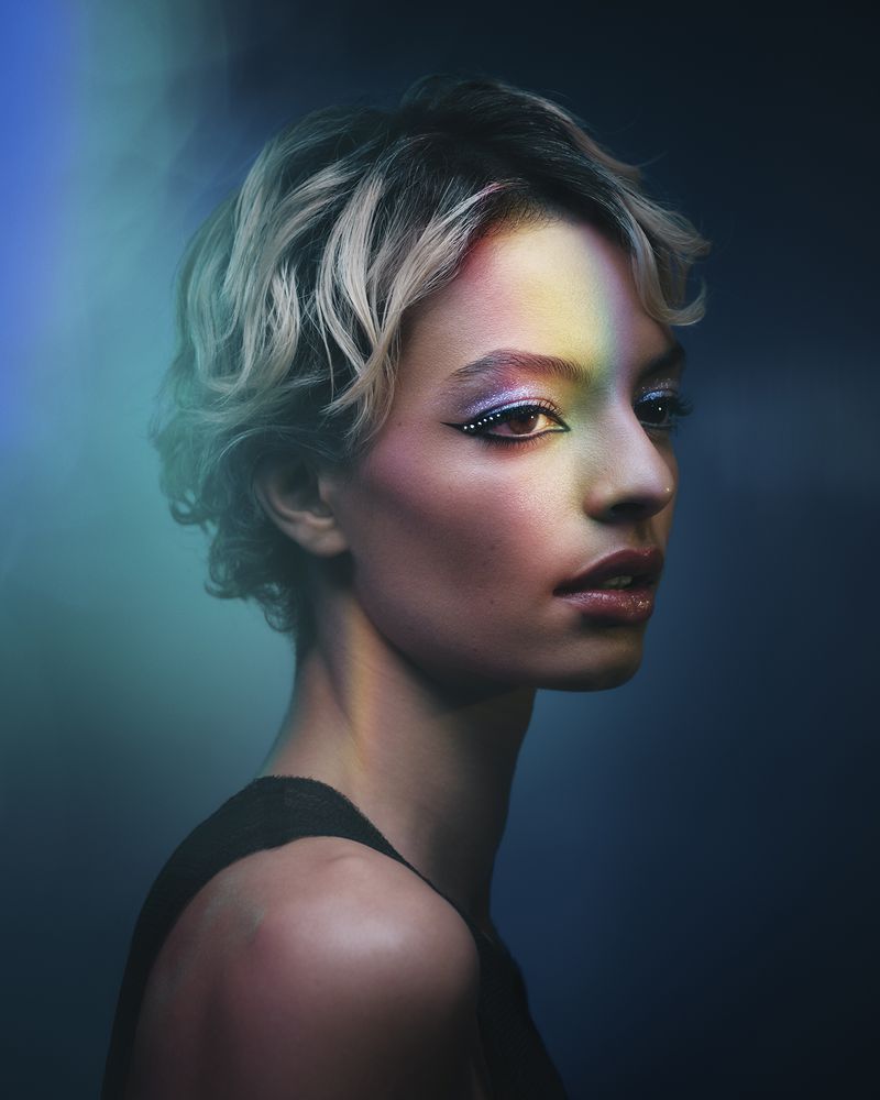 Portrait of a woman with short blonde hair and dramatic eye makeup under colorful moody lighting by Sharif Hamza.