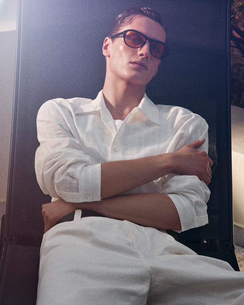 Male model wearing tinted sunglasses and a white shirt against a dark background for the COS campaign