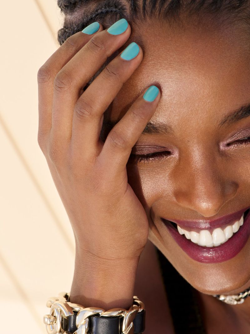 Close-up portrait of Malika Louback smiling with vibrant turquoise nail polish and dark braided hair for Chanel Beauty Les Beiges.