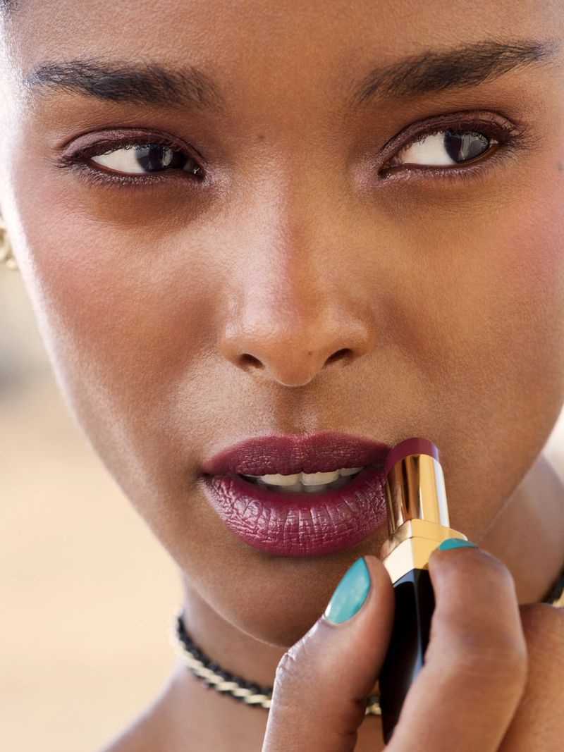 Close-up portrait of model Malika Louback applying deep berry lipstick for Chanel Beauty Les Beiges campaign