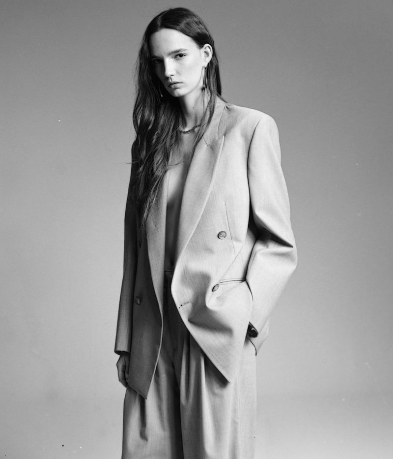 Model wearing an oversized double-breasted blazer and trousers against a neutral grey studio seamless backdrop.