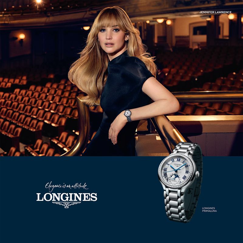 Actor Jennifer Lawrence leaning against a theatre balcony railing wearing a black dress and a silver wristwatch in an advertising campaign.