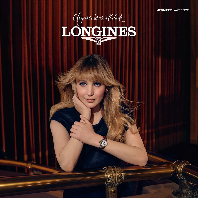 Jennifer Lawrence leaning on a polished brass railing against dark pleated curtains in a portrait photographed by Sharif Hamza.