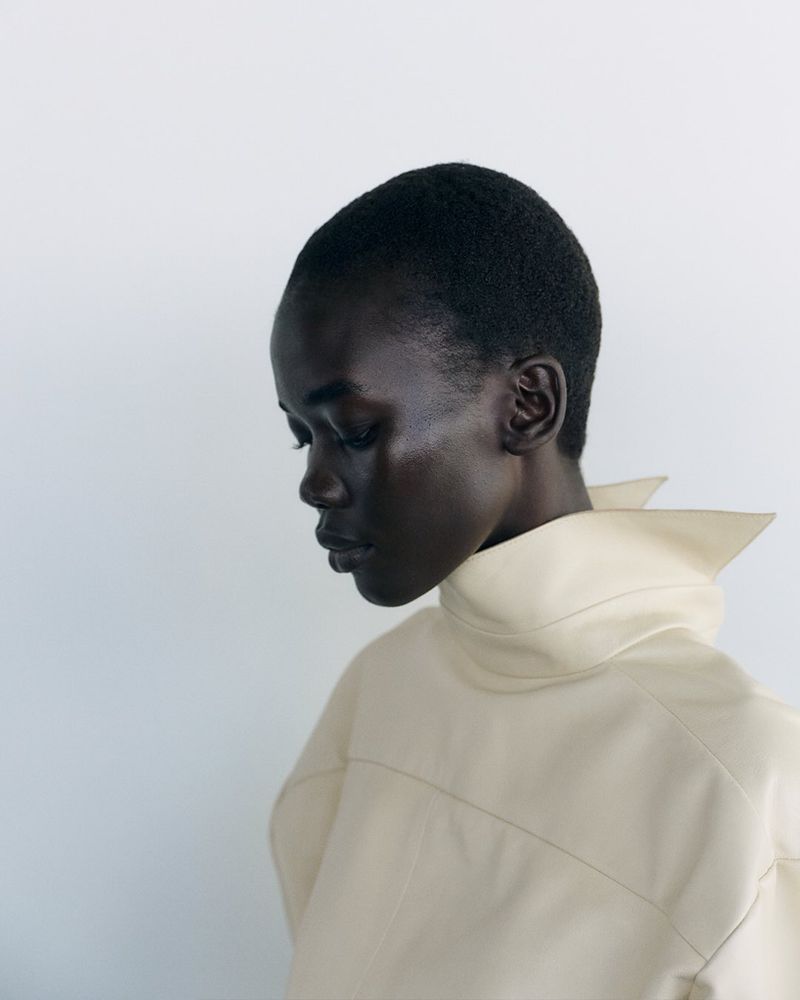 Model with short cropped hair wearing a cream high-collar garment against a plain white background