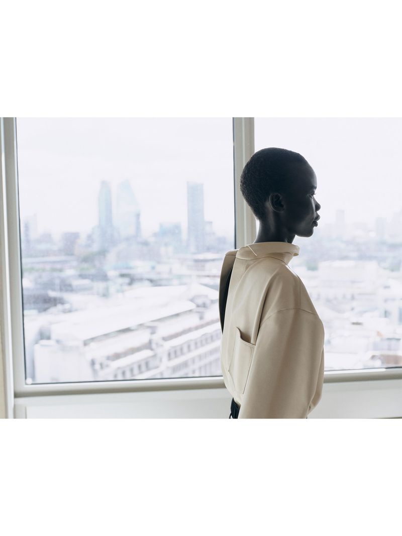 Model in profile wearing a cream top looking out a large window overlooking a city skyline