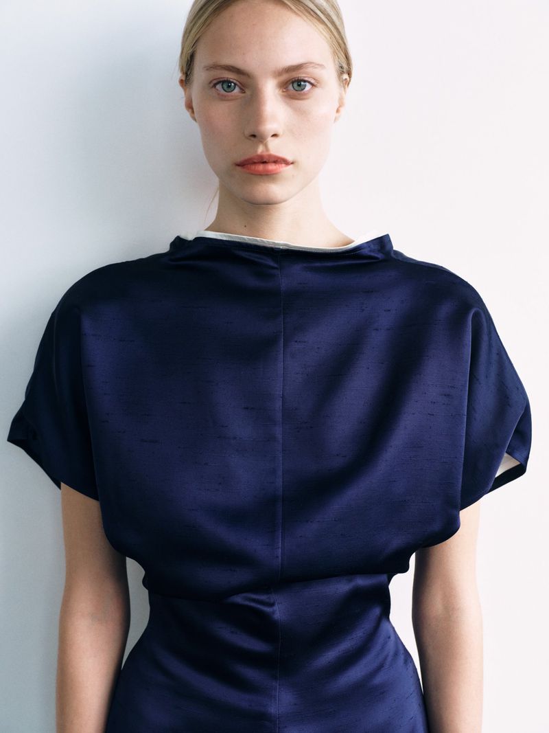 Portrait of a blonde woman wearing a structured navy blue dress against a plain white background.