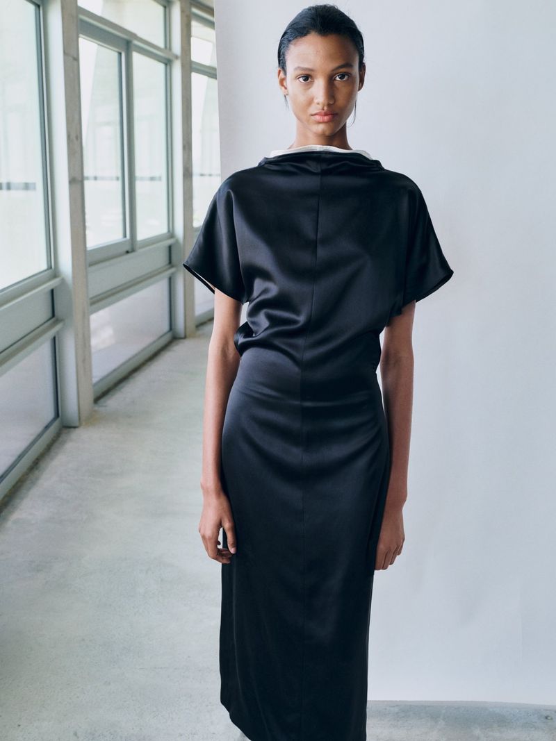 Model in a black satin dress posing in a modern hallway with large windows for Tove S/S 26