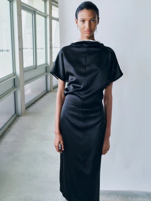 Model in a black satin dress posing in a modern hallway with large windows for Tove S/S 26