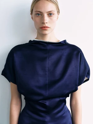 Portrait of a blonde woman wearing a structured navy blue dress against a plain white background.