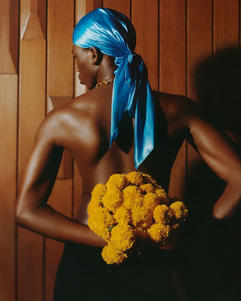 Model wearing bright blue satin durag holding yellow flowers against wooden paneling