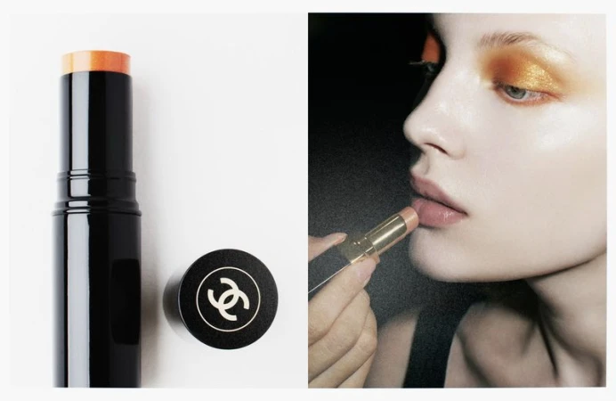 Chanel makeup advertisement featuring a woman applying a golden lipstick with matching eyeshadow on a dark background.