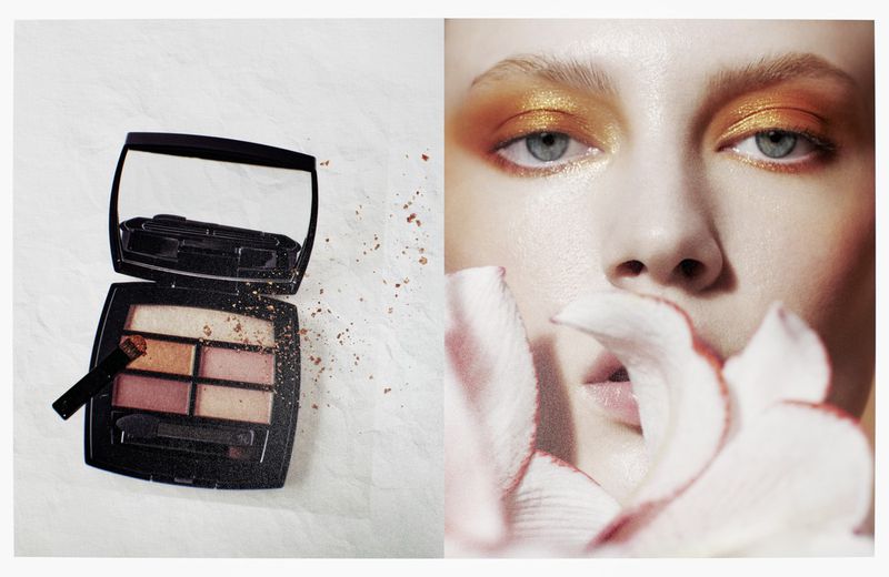 Cosmetic advertisement featuring a palette with applicators and a close-up of a person with gold eyeshadow and white flower petals.