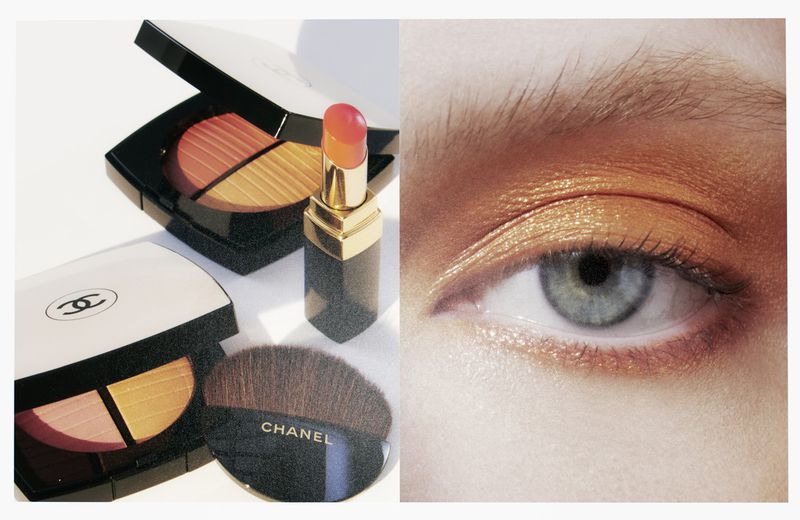 Closeup beauty shot with Chanel makeup: eyeshadow palettes, lipstick, and makeup brush displayed near model's eye with gold eyeshadow.