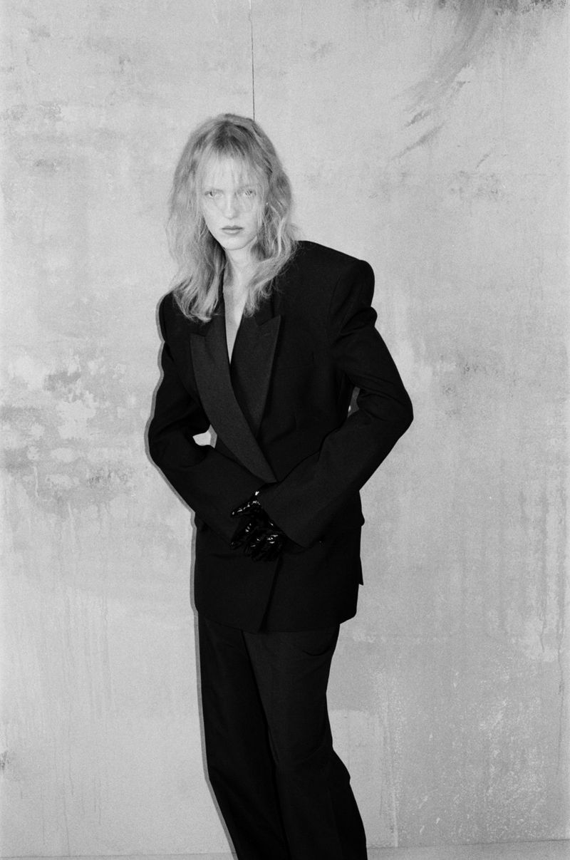 Model in a black suit standing against a textured concrete wall for Cero Magazine BOY editorial