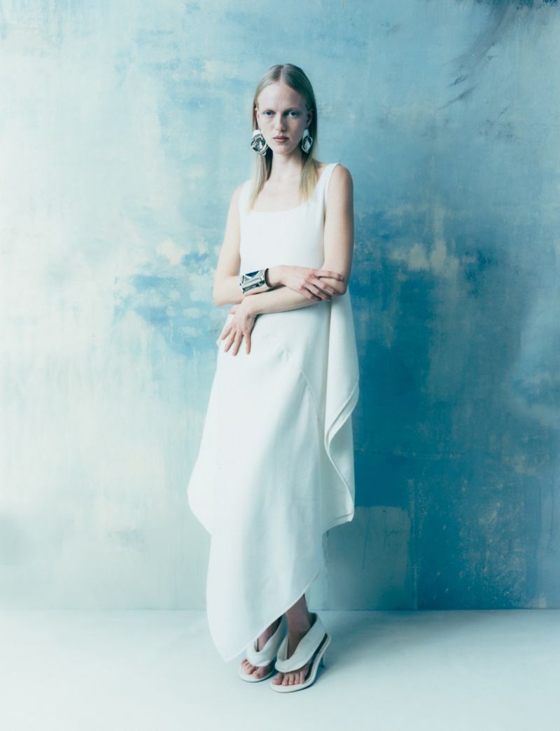 Model in a white dress standing against a textured blue and white painted wall
