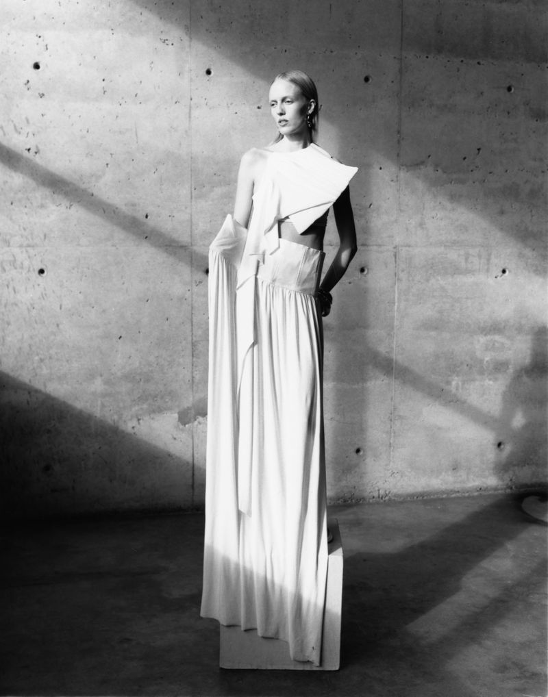 Model standing on a block wearing a draped white architectural dress against a concrete wall in a Cero Magazine editorial by Pierre Crosby.