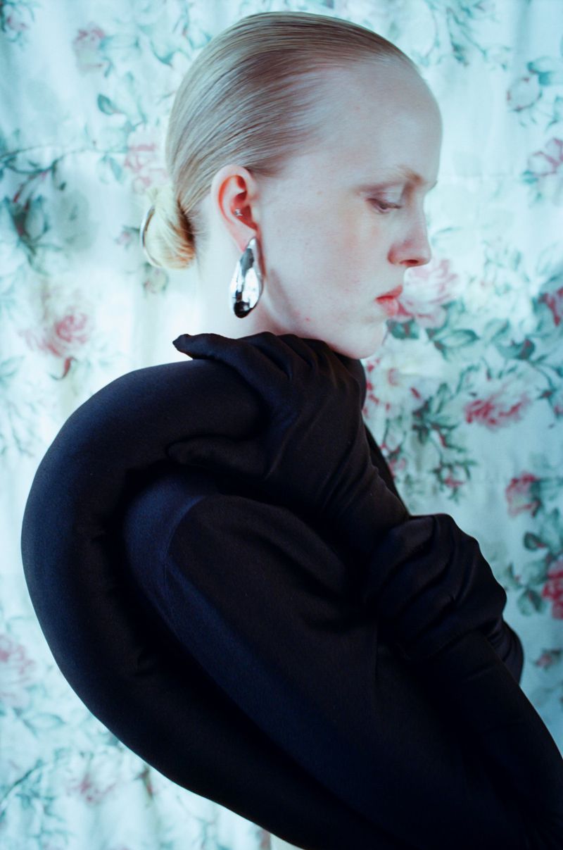 Model in black top with matching gloves and silver earrings posed against floral fabric backdrop for Cero Magazine BOY