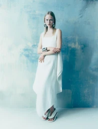 Model in a white dress standing against a textured blue and white painted wall
