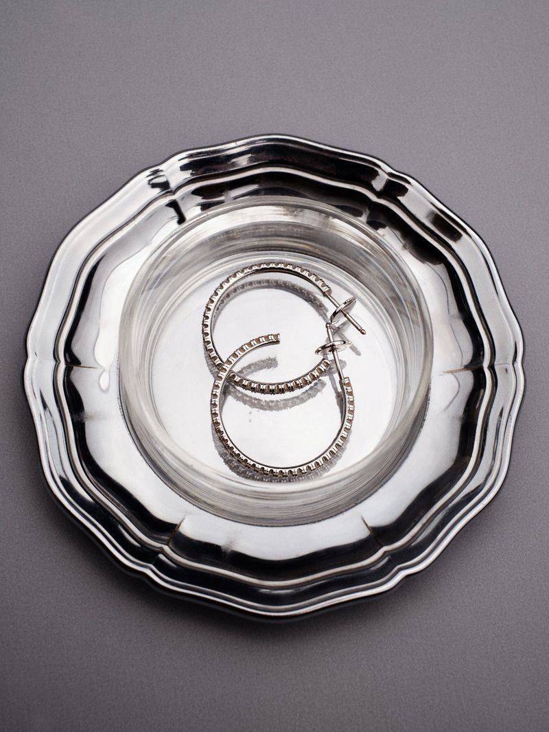 Silver hoop earrings placed inside a small glass dish resting on a metallic tray against a grey background.