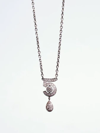 Close-up product shot of a silver diamond-pave number five pendant necklace hanging against a pale background.
