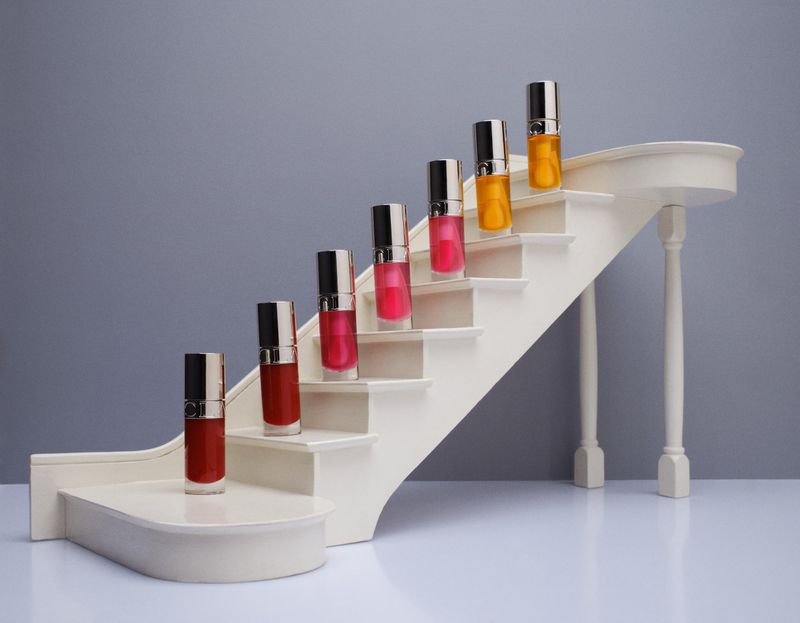 Seven miniature bottles of liquid in a rainbow of colors arranged ascending a small white staircase model.