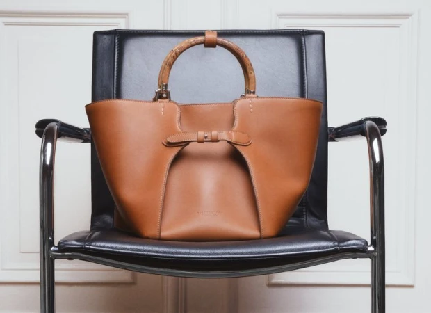 Brown leather handbag with curved wooden handles resting on a black leather office chair