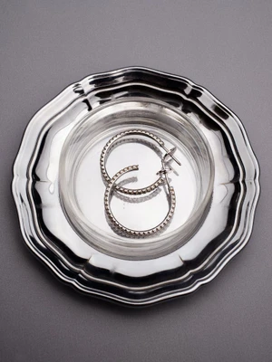 Silver hoop earrings placed inside a small glass dish resting on a metallic tray against a grey background.