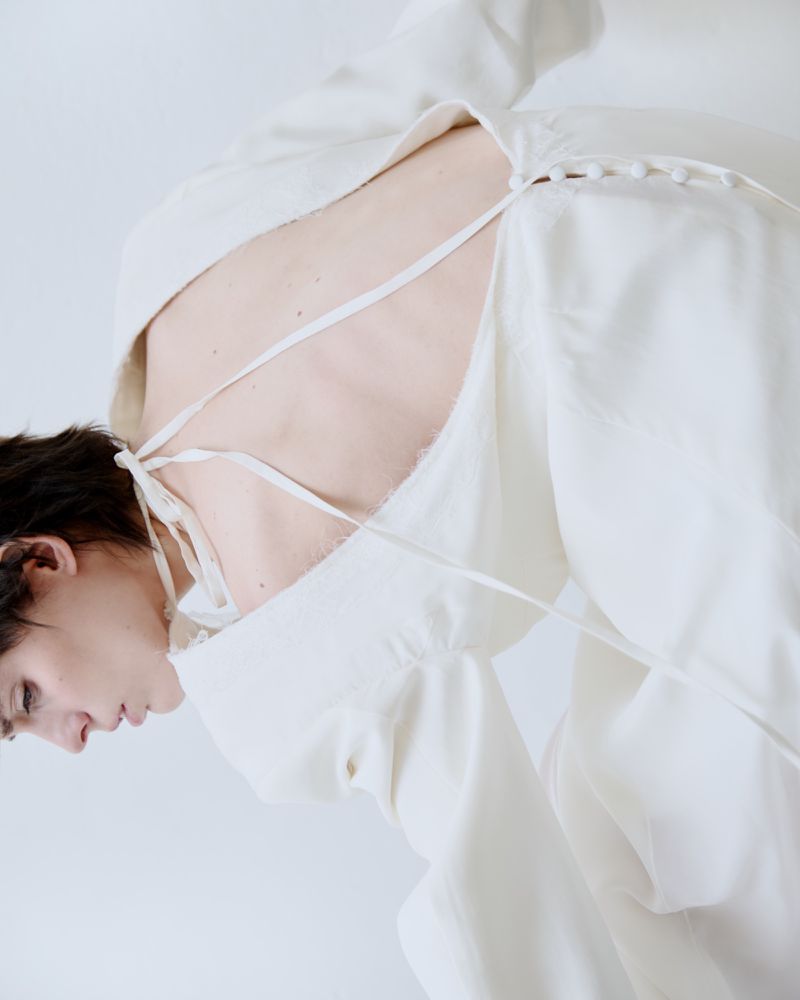 Model wearing a white dress with delicate back ties and button details against a seamless white background