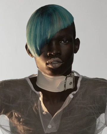 Model with striking blue side-swept hair wearing a white buckled neck collar and sheer textured top against a neutral background.