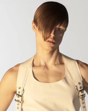Model with slicked-over hair wearing a cream harness top against a bright white background