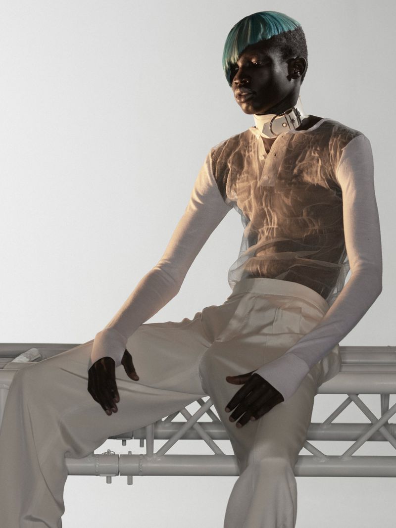 Model with teal hair and white neck collar seated on scaffolding against a bright white background
