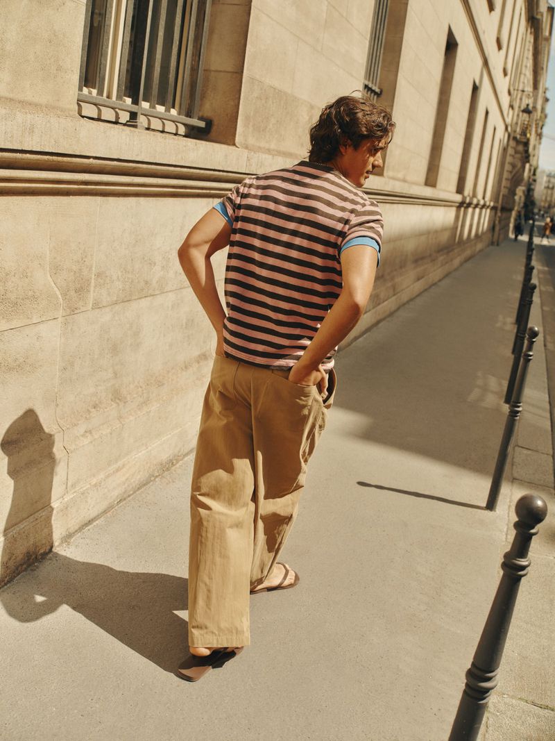 Man walking on a sunny city sidewalk wearing a striped polo shirt and loose khaki trousers