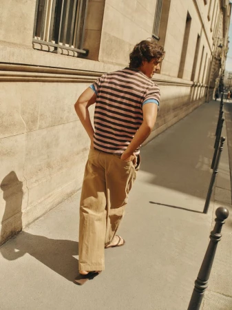 Man walking on a sunny city sidewalk wearing a striped polo shirt and loose khaki trousers