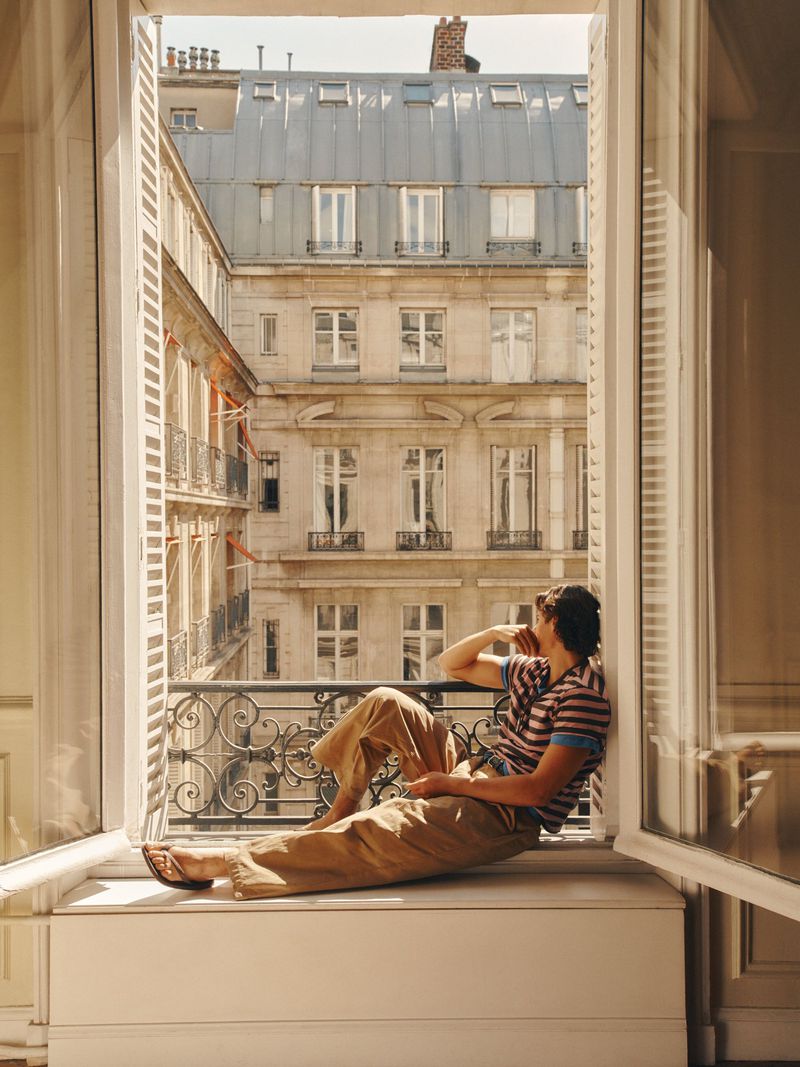 Man sitting on a window sill looking out at Parisian architecture for Zara Summer Cities campaign
