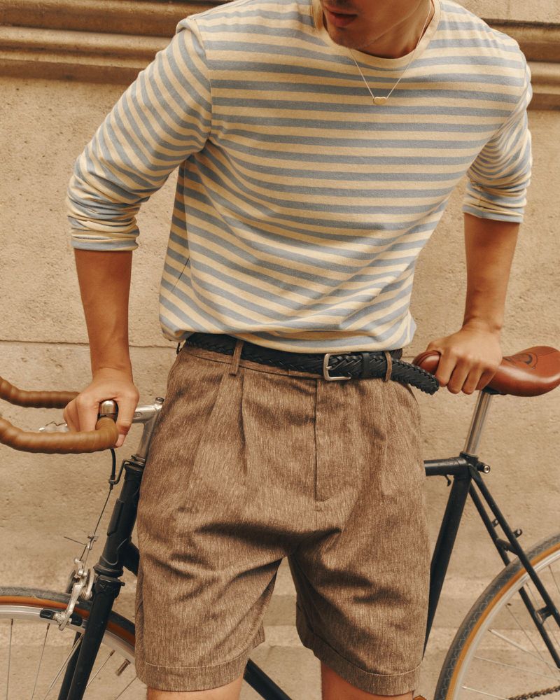 Man wearing a striped long-sleeve t-shirt and brown shorts leaning over a vintage bicycle outdoors