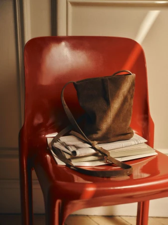 Brown suede handbag resting on a stack of newspapers atop a glossy red chair indoors
