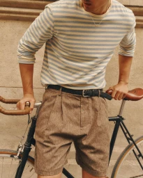 Man wearing a striped long-sleeve t-shirt and brown shorts leaning over a vintage bicycle outdoors