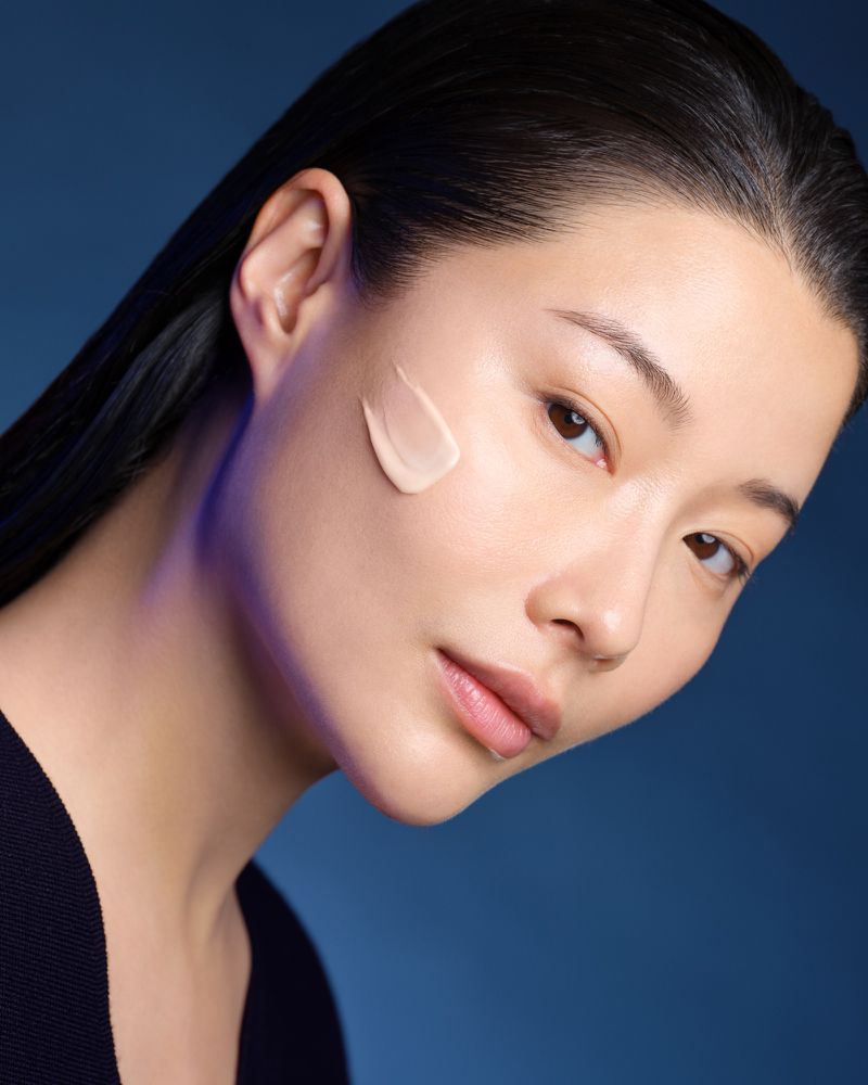 Close-up of an Asian woman with fair skin wearing makeup and posing against a dark blue background in a beauty-style portrait.