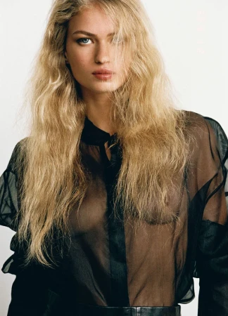 Portrait of a blonde woman wearing a sheer black blouse against a plain light background